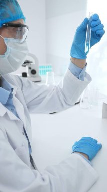 Mavi kapaklı, eldivenli ve Google 'lı tıp bilimi araştırmacısı laboratuvar çalışma alanında test tüpündeki sıvıyı inceliyor. İlaç ve sağlık hizmetleri kavramı.