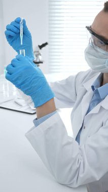 Laboratuvar analizi sırasında cam şişeye kimyasal solüsyon yerleştiren koruyucu giysi araştırmacısı, beyaz arka plan. Tıp, sağlık ve bilim konsepti