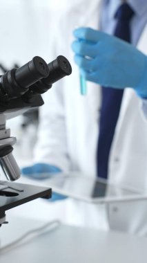 Mikroskop bir masada, steril bir laboratuvar ortamında yenilikçi tıbbi araştırmalar için hazır. Arka planda, bir bilim adamı elde edilen verileri analiz eder. Tıp ve bilim kavramı.