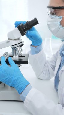 Kadın bilim adamı mikroskop ile numune analiz ediyor, tıbbi araştırma sırasında koruyucu laboratuvar giysileri giyiyor. Tıp, laboratuvar ve bilim konsepti.