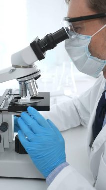 Koruyucu Google ve mavi eldiven giyen bilim adamı mikroskop kullanarak modern laboratuvarda bilimsel araştırmalar yapıyor. Tıp ve bilim konsepti.