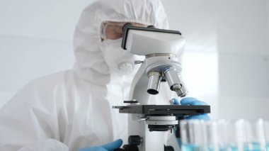 Erkek bilim araştırmacısı ya da virolog koruyucu ekipman takıyor mikroskop ayarlıyor, laboratuvar örneklerini steril araştırma ortamında hassasiyetle analiz ediyor. Tıp konsepti.