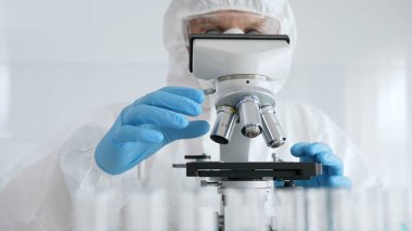 Erkek bilim araştırmacısı ya da virolog koruyucu ekipman takıyor mikroskop ayarlıyor, laboratuvar örneklerini steril araştırma ortamında hassasiyetle analiz ediyor. Tıp konsepti.