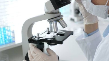 Bilim adamının beyaz eldivenli elleri parlak bir laboratuvarda mikroskobu ayarlıyor, kesinliği vurguluyor ve bilimsel araştırmalara odaklanıyor. Tıp, sağlık ve bilim konsepti.