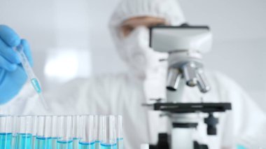 Koruyucu ekipman takan bilim araştırmacısı, tıbbi araştırma deneyi yaparken deney tüplerine sıvıyı dikkatlice yerleştiriyor. Tıp, sağlık ve bilim konsepti.