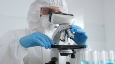 Koruyucu ekipman takan bilim araştırmacısı mikroskobu ayarlıyor, laboratuvar örneklerini steril araştırma ortamında hassasiyetle analiz ediyor. Tıp, sağlık ve bilim konsepti.