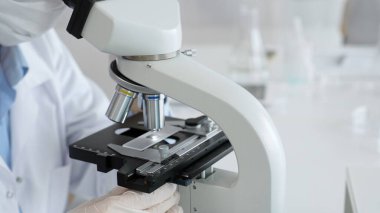 Bilim adamının beyaz eldivenli elleri parlak bir laboratuvarda mikroskobu ayarlıyor, kesinliği vurguluyor ve bilimsel araştırmalara odaklanıyor. Tıp, sağlık ve bilim konsepti.