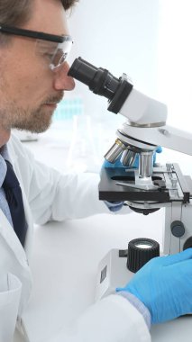 Koruyucu Google ve mavi eldiven giyen bilim adamı mikroskop kullanarak modern laboratuvarda bilimsel araştırmalar yapıyor. Tıp ve bilim konsepti.