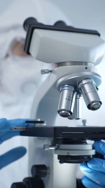 Tehlikeli madde giysisi, maskesi ve eldiveni olan bir tıp virologu bir laboratuvar araştırma virüsünün mikroskobunda özenle çalışıyor. Sağlık ve Bilim Konsepti.
