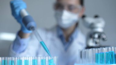 Laboratuvarda test tüplerini mavi bir sıvıyla doldurmak için mikropipetle çalışan bir araştırmacı kadının elini kapatın. Tıp ve Bilim.