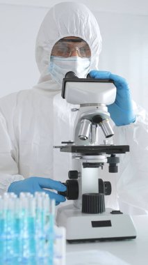 Koruyucu ekipman alanında çalışan bir tıp virologu laboratuvar ortamında araştırma yaparken mikroskop altında virüs örneklerini inceliyor..