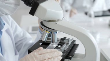 Laboratuar mikroskobunu dikkatlice ayarlayan koruyucu eldivenler giyen bilim teknisyeni titiz bir araştırma tekniği sergiliyor. Tıp, sağlık ve bilim konsepti
