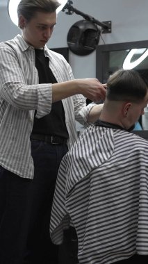 Profesyonel berber müşterilerin saçlarını elektrikli makasla dikkatlice buduyor, modern bir berber dükkanında şık ve kusursuz bir saç kesimi sağlıyor..