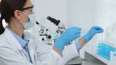 Laboratuvar analizi sırasında cam şişeye kimyasal solüsyon yerleştiren koruyucu giysi araştırmacısı, beyaz arka plan. Tıp, sağlık ve bilim konsepti