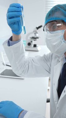 Mavi kapaklı, eldivenli ve Google 'lı erkek bilim araştırmacısı laboratuvar çalışma alanında sıvıyla test tüpünü inceliyor. İlaç ve sağlık hizmetleri kavramı.