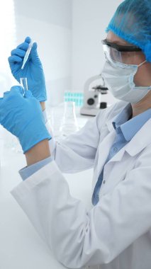 Mavi kapaklı, eldivenli ve Google 'lı tıp bilimi araştırmacısı laboratuvar çalışma alanında test tüpündeki sıvıyı inceliyor. İlaç ve sağlık hizmetleri kavramı.