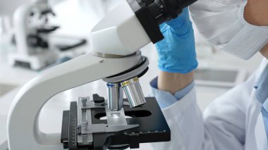 Mikroskop merceklerini inceleyen, detaylı tıbbi laboratuvar araştırmaları yapan mavi eldivenli eldiveni kapatın. Tıp, sağlık ve bilim konsepti.