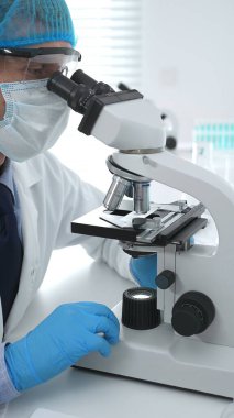 Koruyucu maske takan kıdemli erkek bilim adamı laboratuarda mikroskop kullanarak tıbbi araştırma ve analiz yapıyor. Tıp, sağlık ve bilim konsepti.