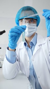 Bilimadamları laboratuvar tıbbi araştırma çalışmaları sırasında koruyucu giysi giyip tüpü hassas pipetle test etmek için kimyasal sıvı eklediler. Tıp, sağlık ve bilim konsepti