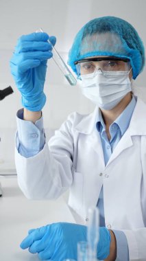 Steril laboratuvar ortamında tıbbi araştırma sırasında mikroskop yakınında mavi sıvı numunesini inceleyen koruyucu ekipman giyen bilim adamları. Tıp, sağlık ve bilim konsepti