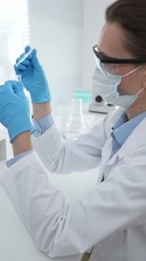 Laboratuvar analizi sırasında cam şişeye kimyasal solüsyon yerleştiren koruyucu giysi araştırmacısı, beyaz arka plan. Tıp, sağlık ve bilim konsepti