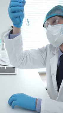 Mavi kapaklı, eldivenli ve Google 'lı erkek bilim araştırmacısı laboratuvar çalışma alanında sıvıyla test tüpünü inceliyor. İlaç ve sağlık hizmetleri kavramı.