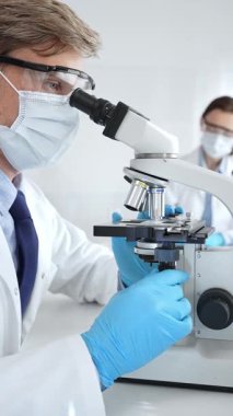 Mikroskop kullanarak maske takan ve eldiven takan bilim adamlarına yakın çekim, modern laboratuvarda araştırmalar yürütmek ve arka planda çalışmak. Tıp, sağlık ve bilim konsepti