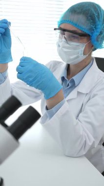 Mavi kapaklı, eldivenli ve Google 'lı tıp bilimi araştırmacısı laboratuvar çalışma alanında test tüpündeki sıvıyı inceliyor. İlaç ve sağlık hizmetleri kavramı.