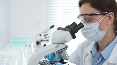 Tıbbi araştırma sırasında steril laboratuvar ortamında çalışırken mikroskop üzerinden numune inceleyen kadın bilim adamı. Tıp, sağlık ve bilim konsepti