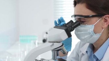 Tıbbi araştırma sırasında steril laboratuvar ortamında çalışırken mikroskop üzerinden numune inceleyen kadın bilim adamı. Tıp, sağlık ve bilim konsepti