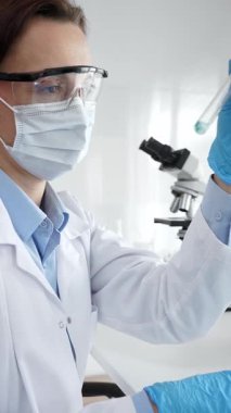 Maske takan ve eldiven takan kadın bilim adamı deney tüpüne sıvı ekliyor. Laboratuvarda tıbbi araştırma için pipet kullanıyor. Tıp, sağlık ve bilim konsepti.