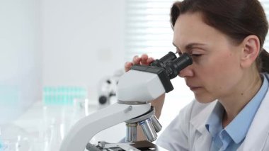 Kadın bilim adamı mikroskop örneklerini analiz ediyor, çağdaş laboratuvar ortamında gelişmiş ekipmanlarla tıbbi tedavileri araştırıyor. Tıp, sağlık ve bilim konsepti