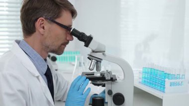 Gelişmiş laboratuvar araştırmaları sırasında mikroskopla biyolojik örnekleri inceleyen odaklanmış bir tıp bilimcisi. Tıp, sağlık ve bilim konsepti