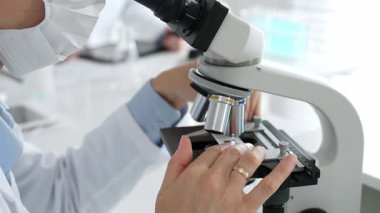 Parlak bir laboratuvarda mikroskobu ayarlarken ellerinizi kapatın ve bilimsel araştırmalara odaklanın. Tıp, sağlık ve bilim konsepti.