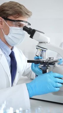 Mikroskop kullanarak maske takan ve eldiven takan bilim adamlarına yakın çekim, modern laboratuvarda araştırmalar yürütmek ve arka planda çalışmak. Tıp, sağlık ve bilim konsepti
