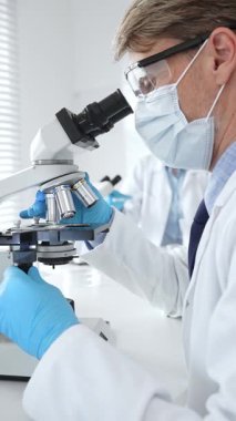 Mikroskop kullanarak maske takan ve eldiven takan bilim adamlarına yakın çekim, modern laboratuvarda araştırmalar yürütmek ve arka planda çalışmak. Tıp, sağlık ve bilim konsepti