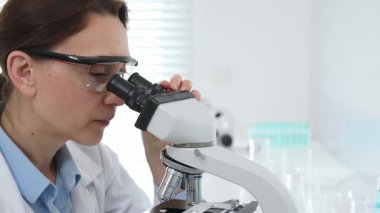Kadın bilim adamı mikroskop örneklerini analiz ediyor, çağdaş laboratuvar ortamında gelişmiş ekipmanlarla tıbbi tedavileri araştırıyor. Tıp, sağlık ve bilim konsepti