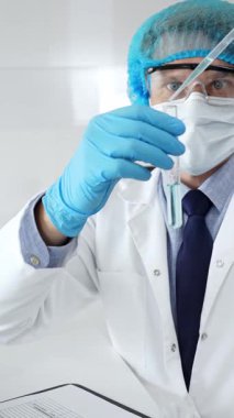 Steril laboratuvar çalışma alanı içindeki pipeti kullanarak turkuaz sıvı örneğini inceleyen koruyucu ekipman giyen bir bilim adamı. Tıp, sağlık ve bilim konsepti