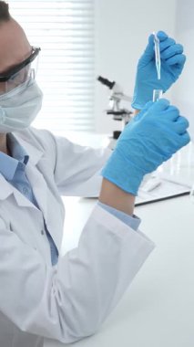 Laboratuvar analizi sırasında cam şişeye kimyasal solüsyon yerleştiren koruyucu giysi araştırmacısı, beyaz arka plan. Tıp, sağlık ve bilim konsepti