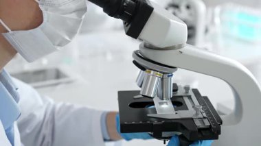 Mikroskop merceklerini inceleyen mavi koruyucu giysiler giyen, detaylı tıbbi laboratuvar araştırmaları yapan bilim adamlarına yaklaş. Tıp, sağlık ve bilim konsepti.