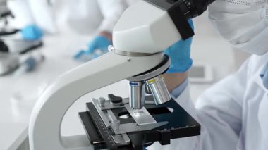 Mikroskop merceklerini inceleyen mavi koruyucu giysiler giyen, detaylı tıbbi laboratuvar araştırmaları yapan bilim adamlarına yaklaş. Tıp, sağlık ve bilim konsepti.