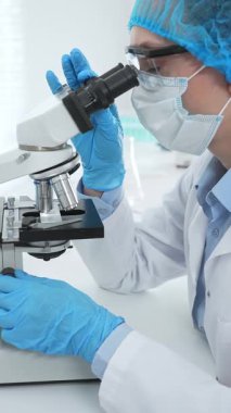 Kadın bilim adamı mikroskop ile numune analiz ediyor, tıbbi araştırma sırasında koruyucu laboratuvar giysileri giyiyor. Tıp, laboratuvar ve bilim konsepti.