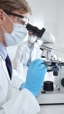 Mikroskop kullanarak maske takan ve eldiven takan bilim adamlarına yakın çekim, modern laboratuvarda araştırmalar yürütmek ve arka planda çalışmak. Tıp, sağlık ve bilim konsepti