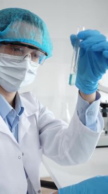 Steril laboratuvar ortamında tıbbi araştırma sırasında mikroskop yakınında mavi sıvı numunesini inceleyen koruyucu ekipman giyen bilim adamları. Tıp, sağlık ve bilim konsepti