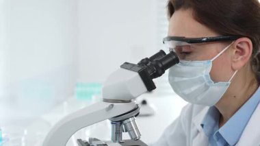 Tıbbi araştırma sırasında steril laboratuvar ortamında çalışırken mikroskop üzerinden numune inceleyen kadın bilim adamı. Tıp, sağlık ve bilim konsepti