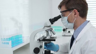 Gelişmiş laboratuvar araştırmaları sırasında mikroskopla biyolojik örnekleri inceleyen odaklanmış bir tıp bilimcisi. Tıp, sağlık ve bilim konsepti