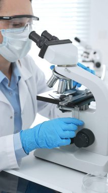 Mavi koruyucu giysili kadın bilim adamı laboratuvar araştırma ortamında test örneklerini mikroskop altında analiz ediyor. Tıp, sağlık ve bilim konsepti.