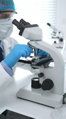 Koruyucu maske takan kıdemli erkek bilim adamı laboratuarda mikroskop kullanarak tıbbi araştırma ve analiz yapıyor. Tıp, sağlık ve bilim konsepti.