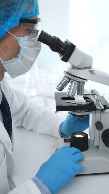 Koruyucu maske takan kıdemli erkek bilim adamı laboratuarda mikroskop kullanarak tıbbi araştırma ve analiz yapıyor. Tıp, sağlık ve bilim konsepti.