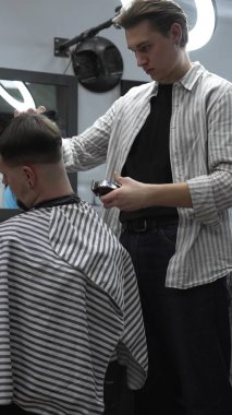 Profesyonel berber müşterilerin saçlarını elektrikli makasla dikkatlice buduyor, modern bir berber dükkanında şık ve kusursuz bir saç kesimi sağlıyor..